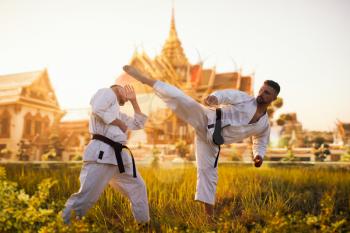 Karate fighters on training fight against ancient temple on sunset. Martial art workout outdoor. Photo manipulation with background