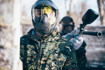 Male paintball player in splattered mask, front view, winter battle. Extreme sport game, soldier in special uniform