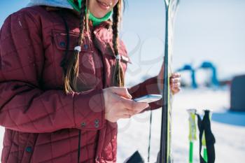 Female skier holds skis and mobile phone in hands. Winter active sport, extreme lifestyle. Downhill or mountain skiing