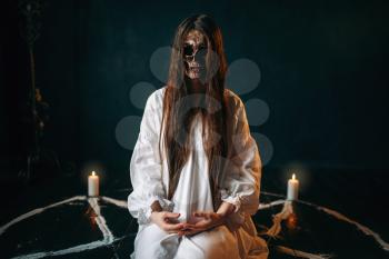 Female witch with skull head sitting in pentagram circle with candles. Dark magic ritual, occult