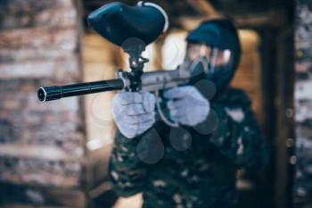 Male paintball player with marker gun in hands, front view, focus on weapon, winter battle. Extreme sport game, soldier fights in protection mask and uniform