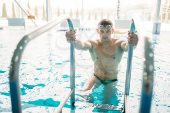 Male swimmer in goggles climbs out of swimming pool. Aqua sport training, healthy lifestyle