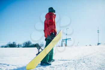 Snowboarder in glasses poses with board in hands, blue sky and snowy mountains on background. Winter active sport, extreme lifestyle, snowboarding