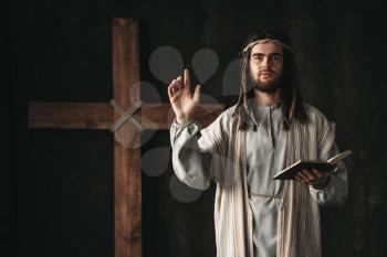Holy Jesus Christ praying with biblical in hands, cross on black background. Prayer against crucifixion, christianity symbol