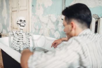 Businessman bankrupt sitting in bathtub against human skeleton, suicide man concept. Problem in business, depression