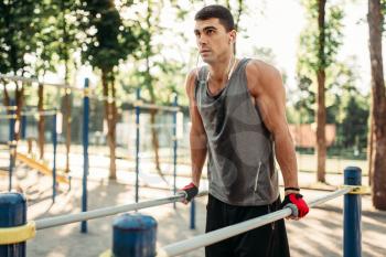 Male athlete in headphones exercises on parallel bars, outdoor fitness workout. Strong sportsman on sport training in park