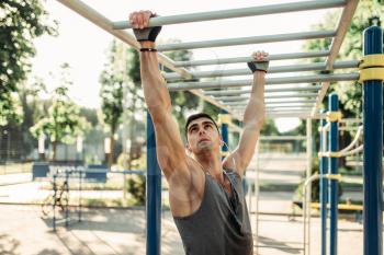 Male athlete training on horizontal bars, outdoor fitness workout. Strong sportsman in summer park