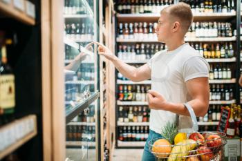 Male customer with basket choosing beer in supermarket. Shopping in food store, alcohol section on background