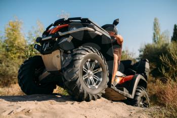 Atv rider climbing the sand mountain in quarry. Male driver in helmet on quad bike in sandpit