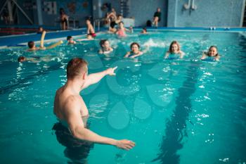 Male instructor works with female class on workout in swimming pool. Aqua aerobics training, water sport