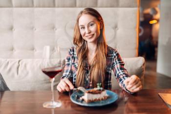 Portrait of young woman in cafe, sweet cake and red wine in a glass on the table. Girl with chocolate dessert in restaurant