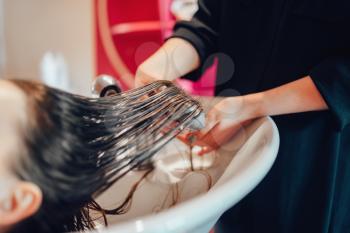 Hairdresser washes customer hair in hairdressing salon. Professional haircare in beauty studio, female client and beautician