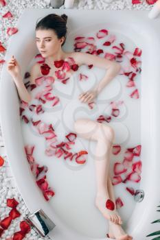 Sexy lady lying in the bath with foam and rose petals, top view. Full relaxation in bathroom