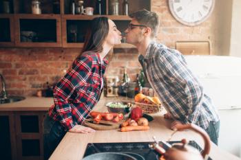 Happy couple kissing while preparing a romantic dinner. Vegetable salad preparation. Family prepares healthy food on the kitchen