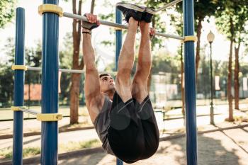 Athletic man doing stretching exercise using horizontal bar, outdoor fitness workout. Strong sportsman on sport training in park