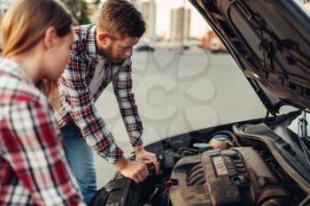 Car breakdown concept, sad couple against open hood. Female driver and mechanic of emergency service looks at the broken vehicle engine