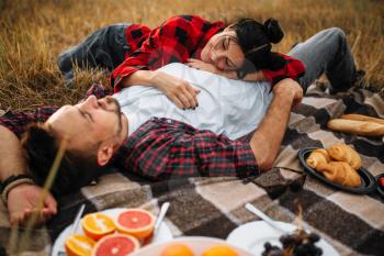 Love couple lies on plaid, picnic in summer field. Romantic junket of man and woman