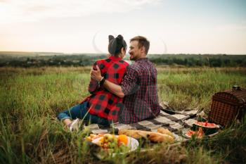 Love couple sitting on plaid, back view, picnic in summer field. Romantic junket, man and woman leisure together