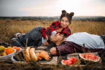 Love couple lies on plaid, fruit picnic in summer field. Romantic junket of man and woman