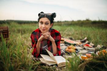 Young woman with book lies on plaid, picnic in summer field. Romantic junket, happy holiday