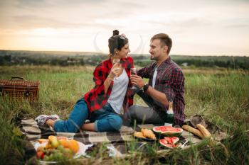Love couple drinks wine, picnic in summer field. Romantic junket, man and woman leisure together, happy family weekend
