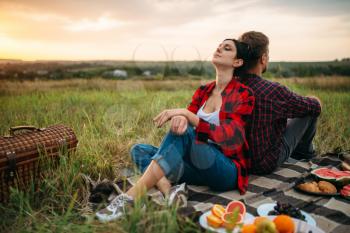 Man and woman sitting with their backs to each other on sunset, picnic in the field. Romantic junket on sunset, couple on outdoor dinner,  happy relationships