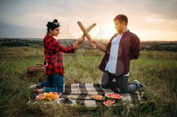 Playful couple fight on loaves, picnic in the field. Romantic junket, man and woman on outdoor dinner, happy relationship