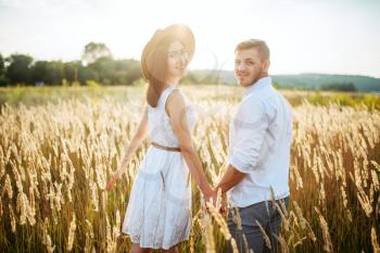 Love couple hold hands, walking in a rye field. Cute family on summer meadow
