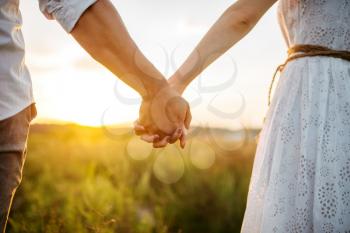 Couple hold hands in green field on sunset. Cute family on summer meadow, happy relationships