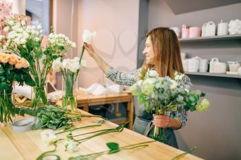 Female florist places flowers in vases, fresh bouquet preparation process. Floral business owner at workplace