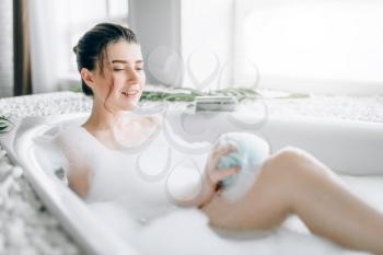 Young woman sitting in the bathroom and soaps the body with a sponge. Luxury bathroom