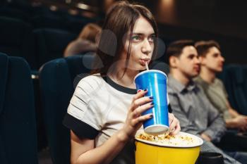Young woman with beverage and popcorn sitting in cinema. Showtime, movie watching 