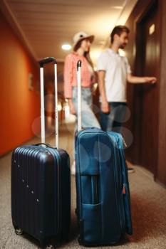 Suitcases in hotel hallway, couple open the door of the hotel room on background. Travelling or tourism concept. Tourists with bags in corridor