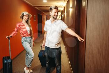 Happy couple with suitcases looking for their hotel room. Travelling or tourism concept, summer vacation