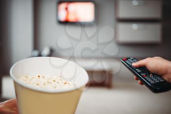 Male hands with television remote control and popcorn against TV on the wall. Home entertainment concept