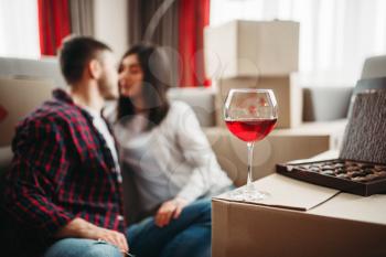 Love couple drinks red wine between cardboard boxes and celebrate moving to new house. Relocation to apartment celebration