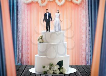 Wedding cake with bride and groom figures on the top, marriage proposal. Sweet pie for newlyweds with little figurines