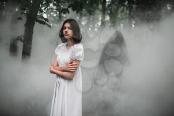 Young female victim in white dress in the misty forest. Photo in horror style, mystery