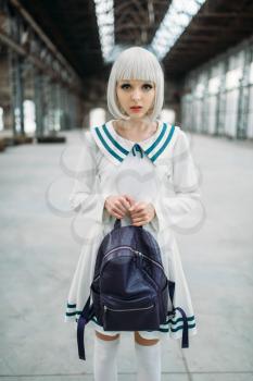 Anime style blonde girl hugs teddy bear. Cosplay woman, japanese culture, doll with toy on abandoned factory