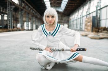 Anime style blonde woman with sword. Cosplay fashion, japanese culture, doll with blade on abandoned factory