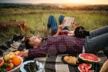 Love couple resting together, picnic in the field. Romantic junket on sunset, man and woman on outdoor dinner, happy family