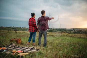 Young couple looking into the distance, picnic in the field. Romantic junket, man and woman on outdoor dinner
