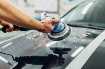 Worker with polishing machine cleans car hood. Auto detailing on carwash service