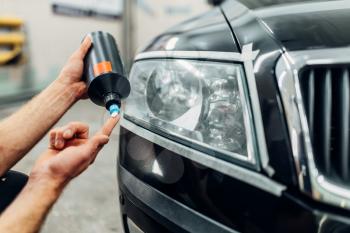 Auto detailing of car headlights on carwash service. Man smears polishing paste