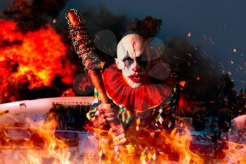 Crazy bloody clown with baseball bat, airplane in fire on background. Man with makeup in halloween costume, scary killer