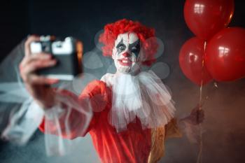 Scary bloody clown with crazy eyes makes selfie. Man with makeup in carnival costume, mad maniac