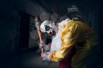 Scary bloody clown with crazy eyes holds baseball bat. Man with makeup in carnival costume, mad maniac