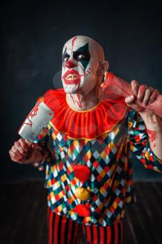 Mad bloody clown with meat cleaver and baseball bat, circus horror. Man with makeup in carnival costume, mad maniac