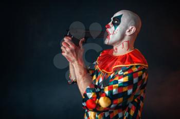 Mad bloody clown with a gun in his mouth, circus horror. Man with makeup in carnival costume, crazy maniac