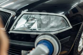 Auto detailing of car headlights on carwash service. Man works with polishing machine